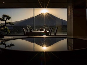 A dining area with a table and chairs, a glass table reflecting the view of a mountain and the sun. - Fuji Mihana Resort (Oyama)