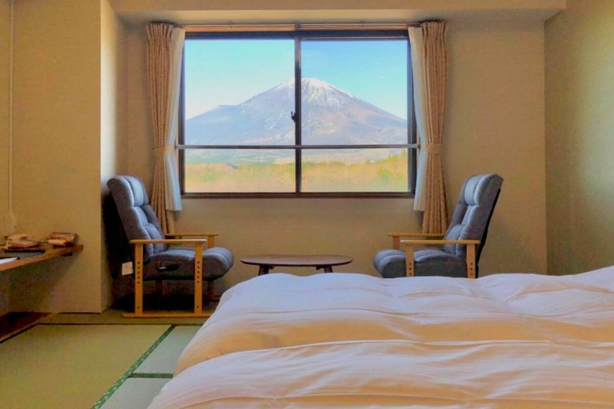 Camera d'albergo con un letto, due poltrone, un tavolino e una finestra vista montagna.