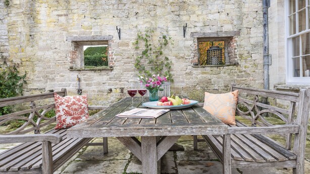 A rustic wooden table with a plate of fruit, a vase of flowers, and two wine glasses. - The Courtyard House, Dorchester (Dorchester)