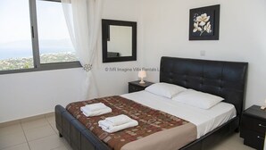 A bedroom with a bed, a nightstand, a mirror, and a window with a view.