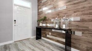 A modern hallway with a white door, a black console table with decorative items, and a wall with wooden paneling and reflective strips. - Ultimate New 8 Bedroom 5 Bathroom Champions Gate Resort Property with Spa and Pool (Davenport)