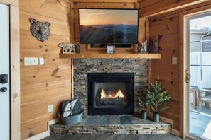 A wooden interior with a fireplace, a television mounted above it, and a stone wall.