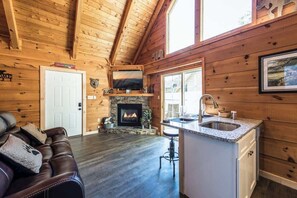 Ein Ferienhaus-Interieur mit Kamin, Holzwänden, einer Couch und einer Küchenzeile.