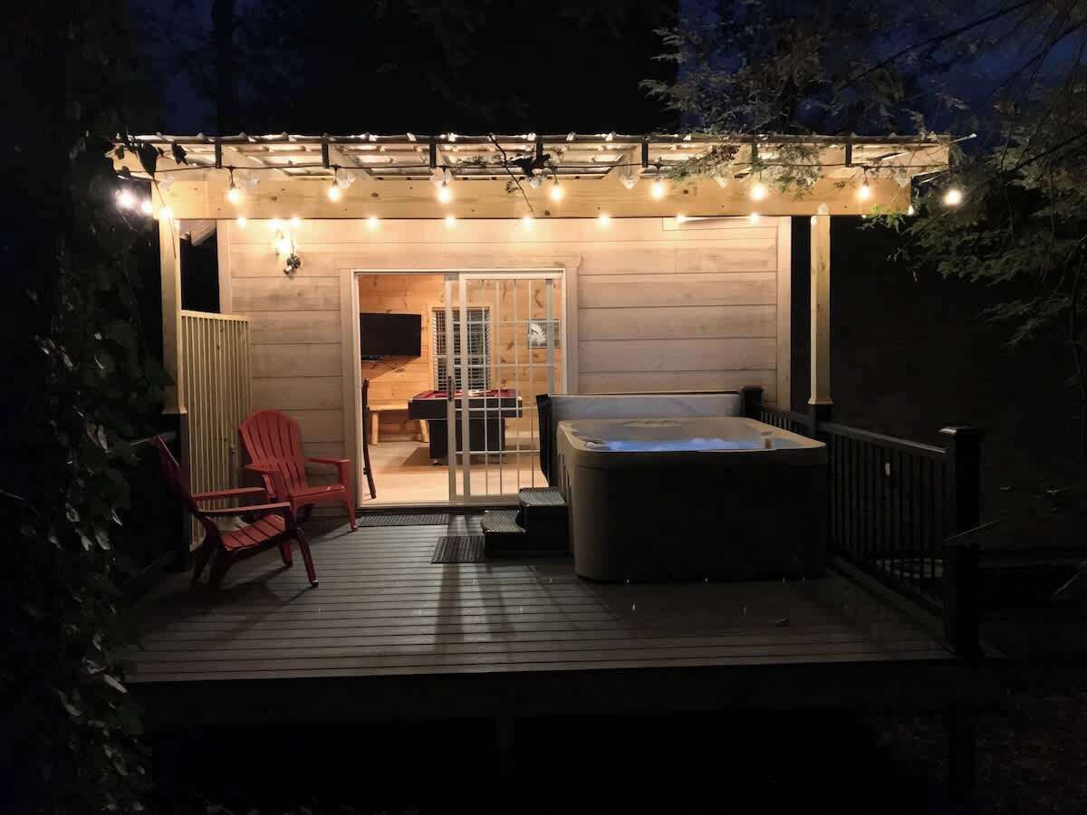 Une terrasse en bois avec un jacuzzi, des sièges d’extérieur et des guirlandes lumineuses.