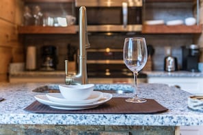 A kitchen counter with a modern faucet, a wine glass, and white dishes.