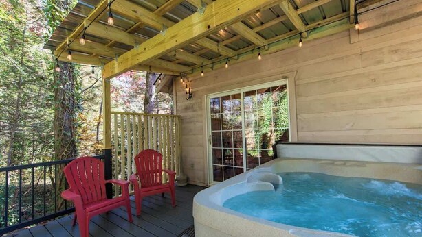 En træterrasse med jacuzzi, to røde stole og et vindue med udsigt over en skov.