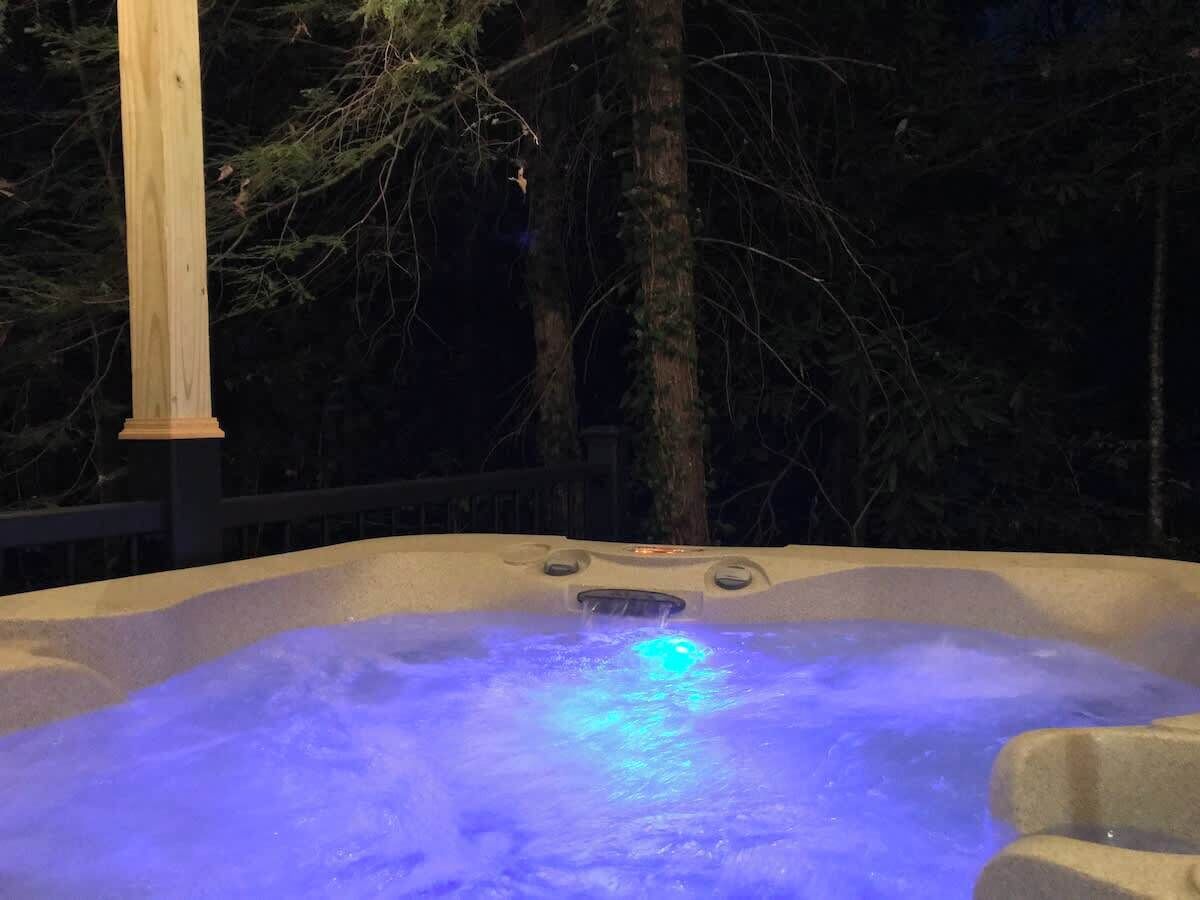 Ein Whirlpool mit blauem Licht, umgeben von Bäumen und einer Holzterrasse.