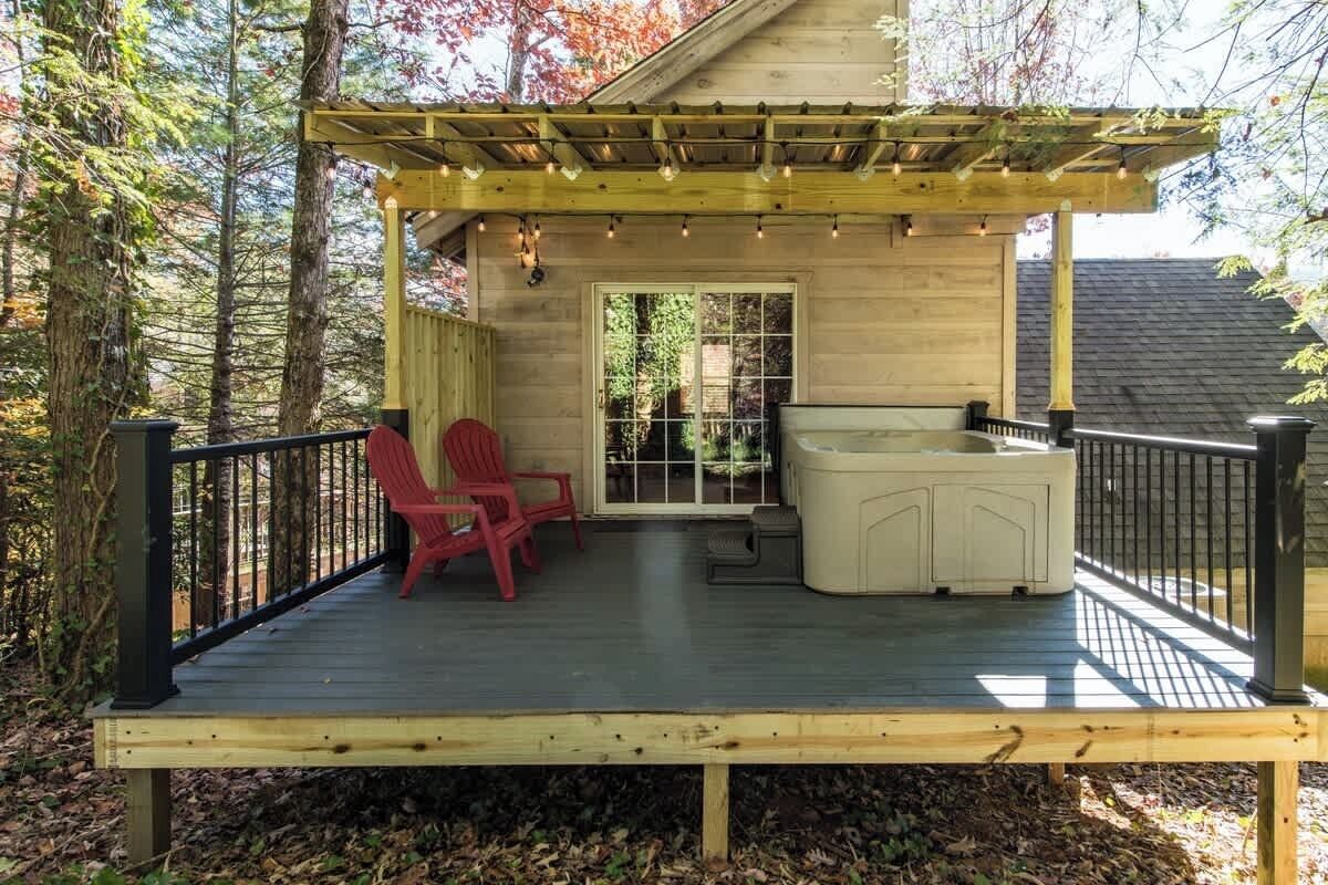 Una terraza de madera con una pérgola, dos sillas rojas y una zona de estar exterior blanca.
