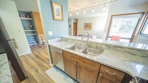 A kitchen with wooden cabinets, a marble countertop, and a stainless steel sink. - Quiet Condo w/Wood Fireplace Near Trails (Keystone)