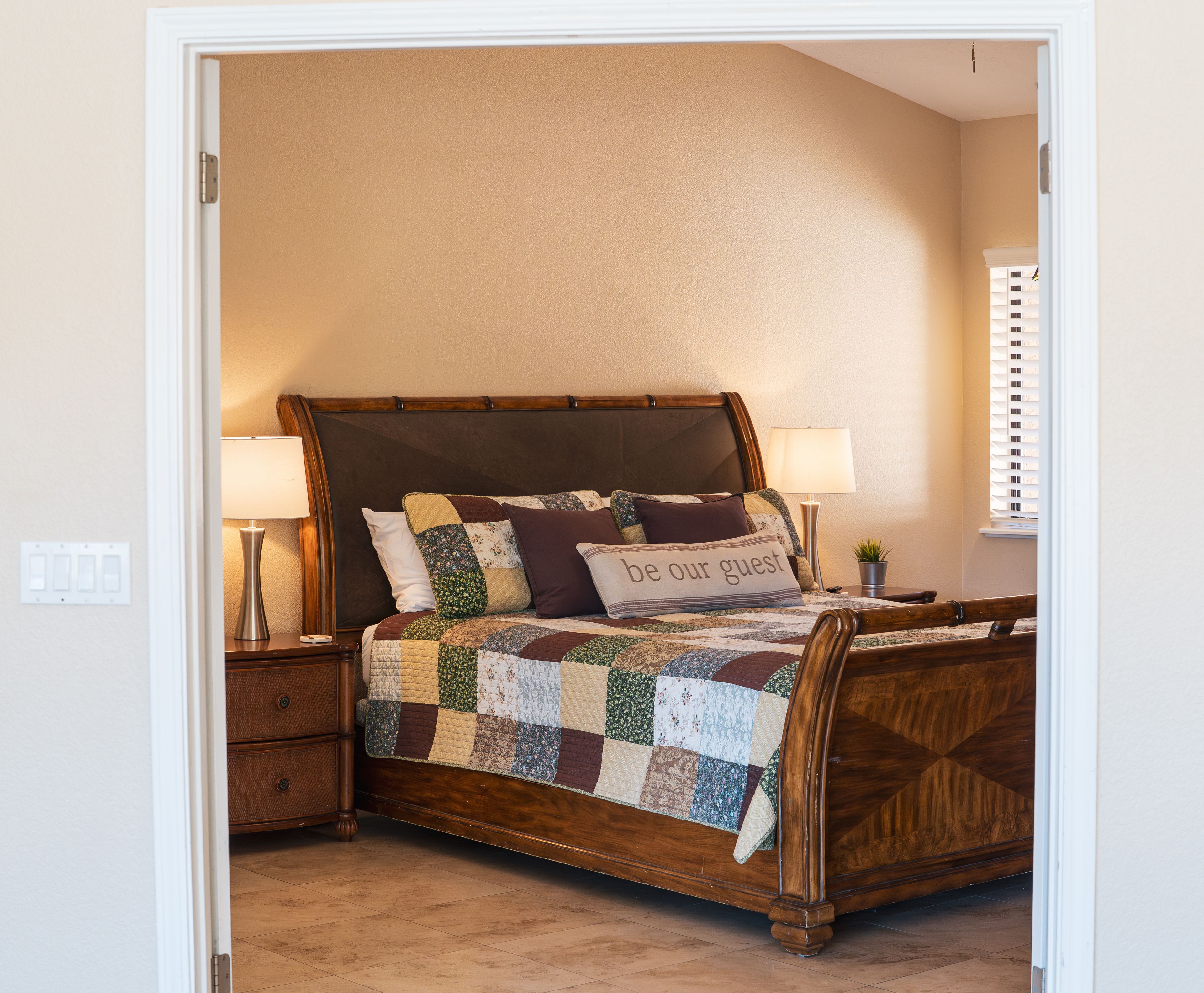 Un dormitorio con una cama de madera, dos lámparas de noche, una mesita de noche y una colcha acolchada.