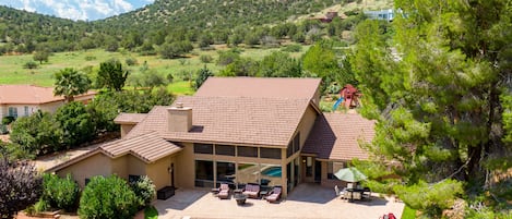 A house with a swimming pool, patio furniture, and a view of a hilly landscape.