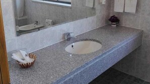 Un baño con encimera de granito, un lavamanos, un espejo y una ventana.