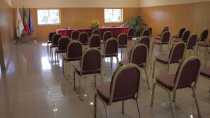 Un salón de conferencias con filas de sillas, una mesa con mantel rojo y banderas en la pared.