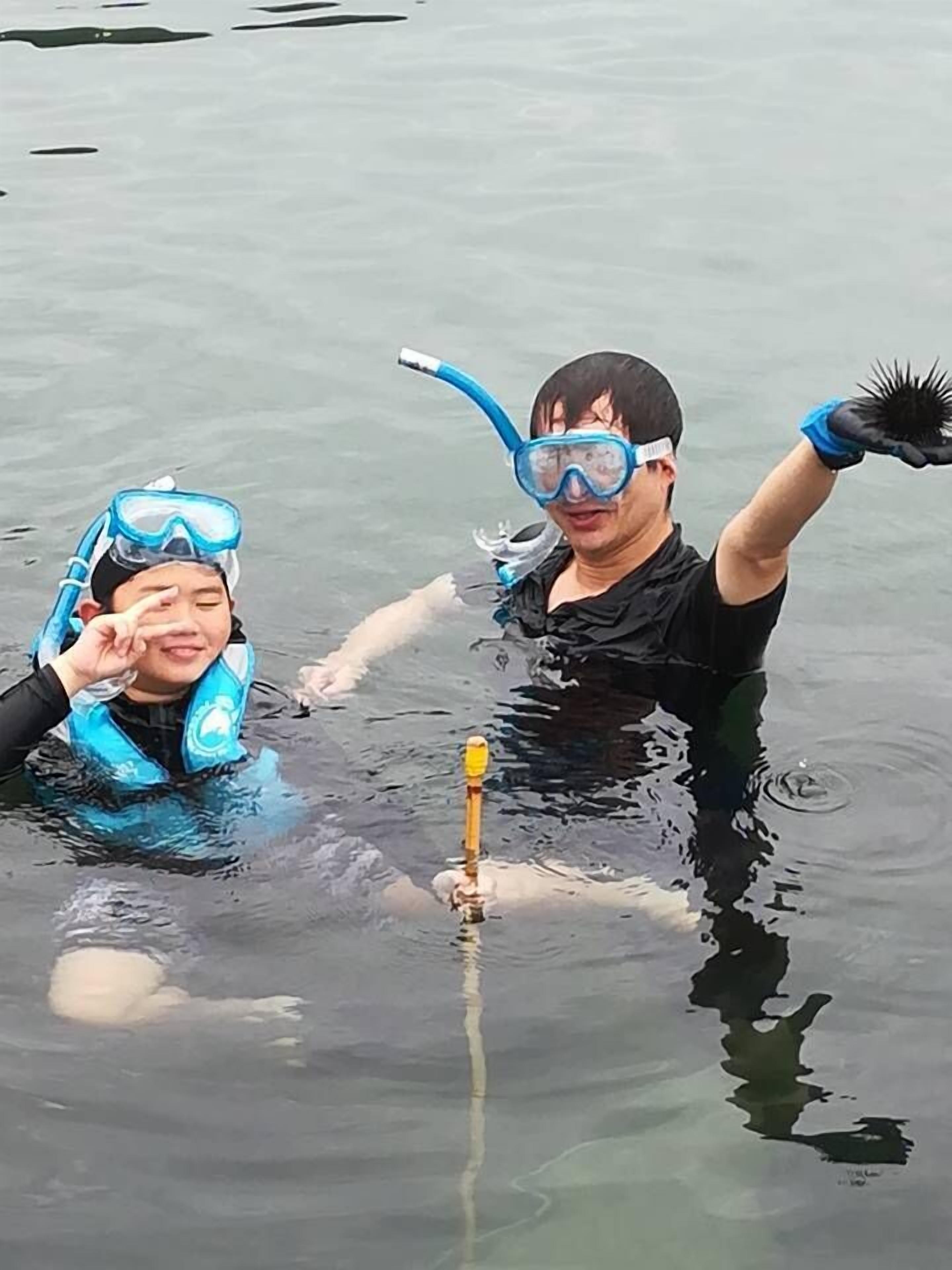 Two people in a body of water, one holding a snorkel and mask, and the other wearing a snorkel mask.