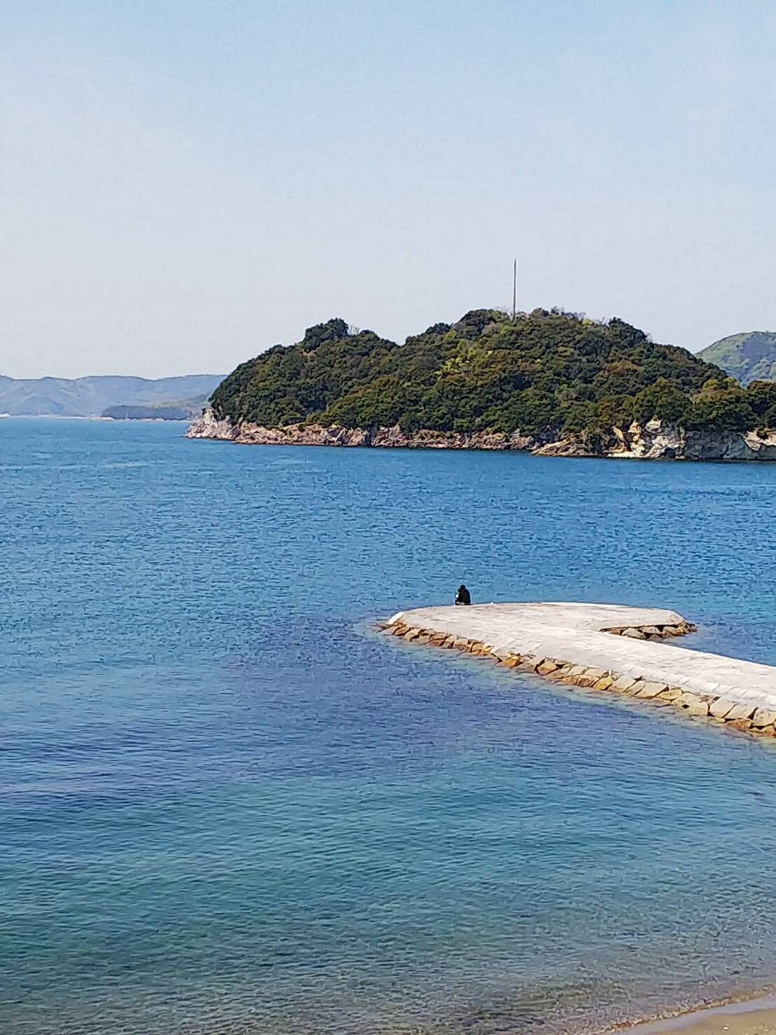 Un paysage côtier avec un promontoire rocheux et une personne assise dessus.