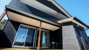 A modern house with large sliding glass doors, a wooden deck, and a small outdoor kitchen area.
