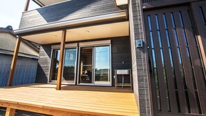 A modern two-story building with a wooden deck, large sliding glass doors, and a dark-colored exterior.