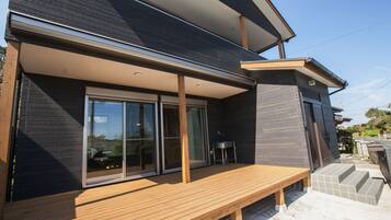 A modern house with a wooden deck, large sliding glass doors, and a small outdoor table.