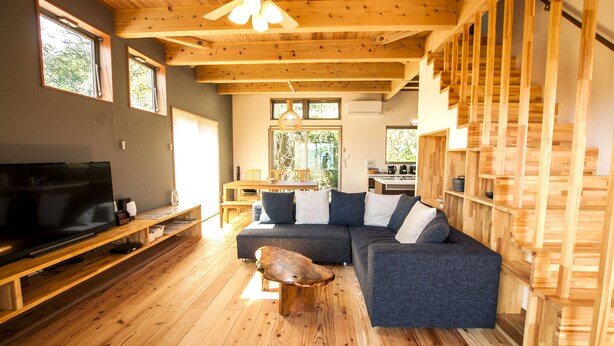 A modern living room with a large sectional sofa, wooden flooring, a flat-screen TV, and built-in wooden shelving.