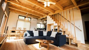 A modern living room with a wooden ceiling, a dark sofa, a wooden coffee table, and a staircase with wooden railings.