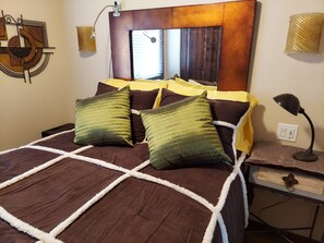 Ein ordentlich bezogenes Bett mit einer braun-weiß gestreiften Tagesdecke, grünen Kissen und einem Holzkopfbrett.