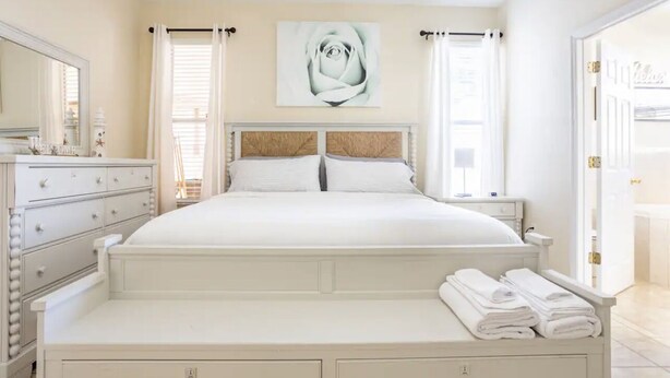 Une chambre à coucher avec un grand lit, une commode, une table de chevet et une œuvre d’art représentant une rose, accrochée au mur.