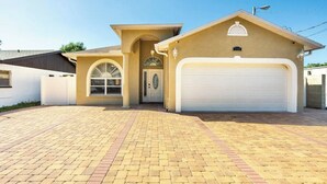 Une maison de plain-pied à l’extérieur beige, avec une porte de garage blanche et une allée pavée en briques.