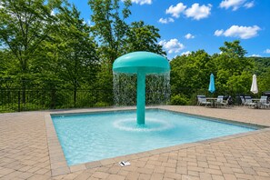 Una piscina con elemento centrale d'acqua, circondata da un solarium in mattoni, alberi e mobili da esterno.