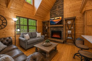 A cozy cabin interior with a fireplace, wooden walls, a sofa, and a dining area. - Top Resort with 3 Pools/Pickleball/Hot Tub/Games (Gatlinburg)