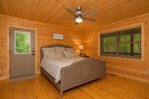 Camera da letto in una baita di legno, con un letto, una ventola a soffitto, una finestra con persiane e una porta.