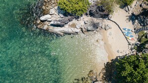 Ein Strand mit klarem Wasser, felsigem Ufer und Kajaks.