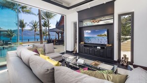 Ein modernes Wohnzimmer mit großem Fernseher, gemütlichen Sitzmöglichkeiten und Blick auf den Ozean.