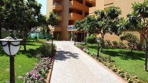 A pathway leading to a building with multiple balconies, surrounded by well-maintained greenery and flower beds. - Merlin Beach Park Hotel (Alanya)