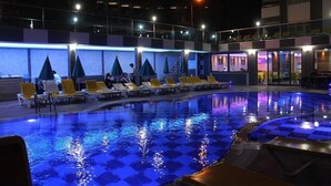 A swimming pool with lounge chairs and umbrellas, surrounded by a building with multiple floors and balconies. - Merlin Beach Park Hotel (Alanya)