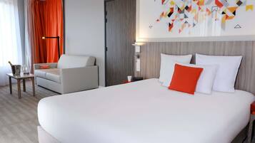A hotel room with a large bed, a sofa, a nightstand, and a wall-mounted lamp.