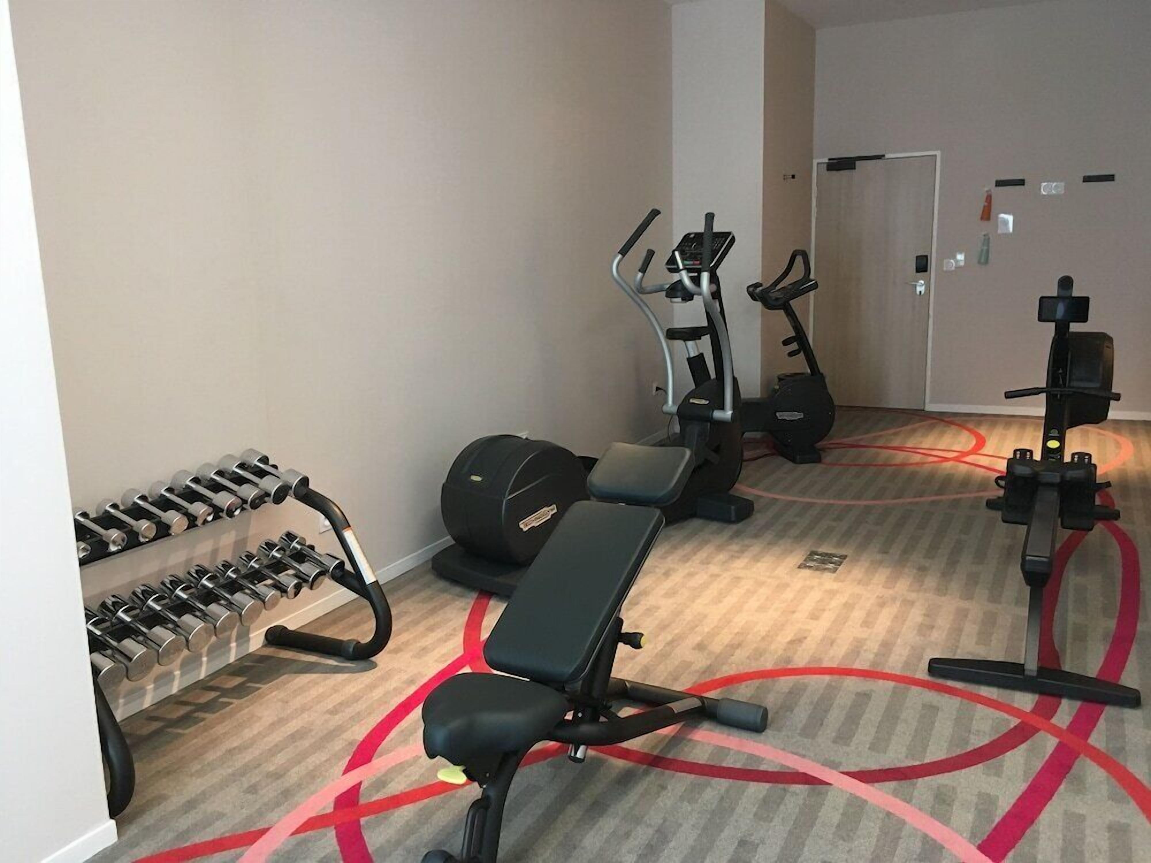 Uma academia com equipamentos de ginástica, incluindo halteres, um banco e aparelhos cardiovasculares.