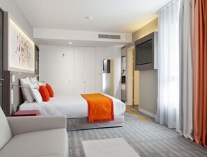 A modern hotel room with a bed, a TV, a sofa, and a large window with curtains. - Hotel Mercure Toulouse Sud (Toulouse)