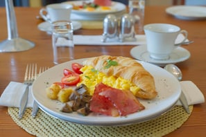 Un plato de desayuno con huevos, jamón, tomates y un croissant sobre una mesa.