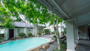 A swimming pool with a stone border, surrounded by potted plants and trees. - Lovely Spacious Room With Breakfast on one of our top Picks in Pretoria (Pretoria)
