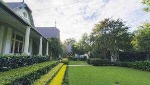 A well-maintained garden with a lawn, hedges, and a building with a grey roof and white columns. - Lovely Guesthouse in Pretoria Welcoming you on a Spacious Room With Breakfast (Pretoria)