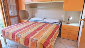 Un lit avec une couverture colorée, une lampe de chevet et une petite commode.