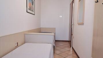 A small, clean room with a single bed, a bedside table, a mirror, and a door.