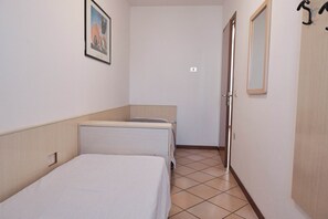 A small, clean room with a single bed, a bedside table, a mirror, and a door. - Cozy Flat in a Bright Residence-beahost (Rosolina)