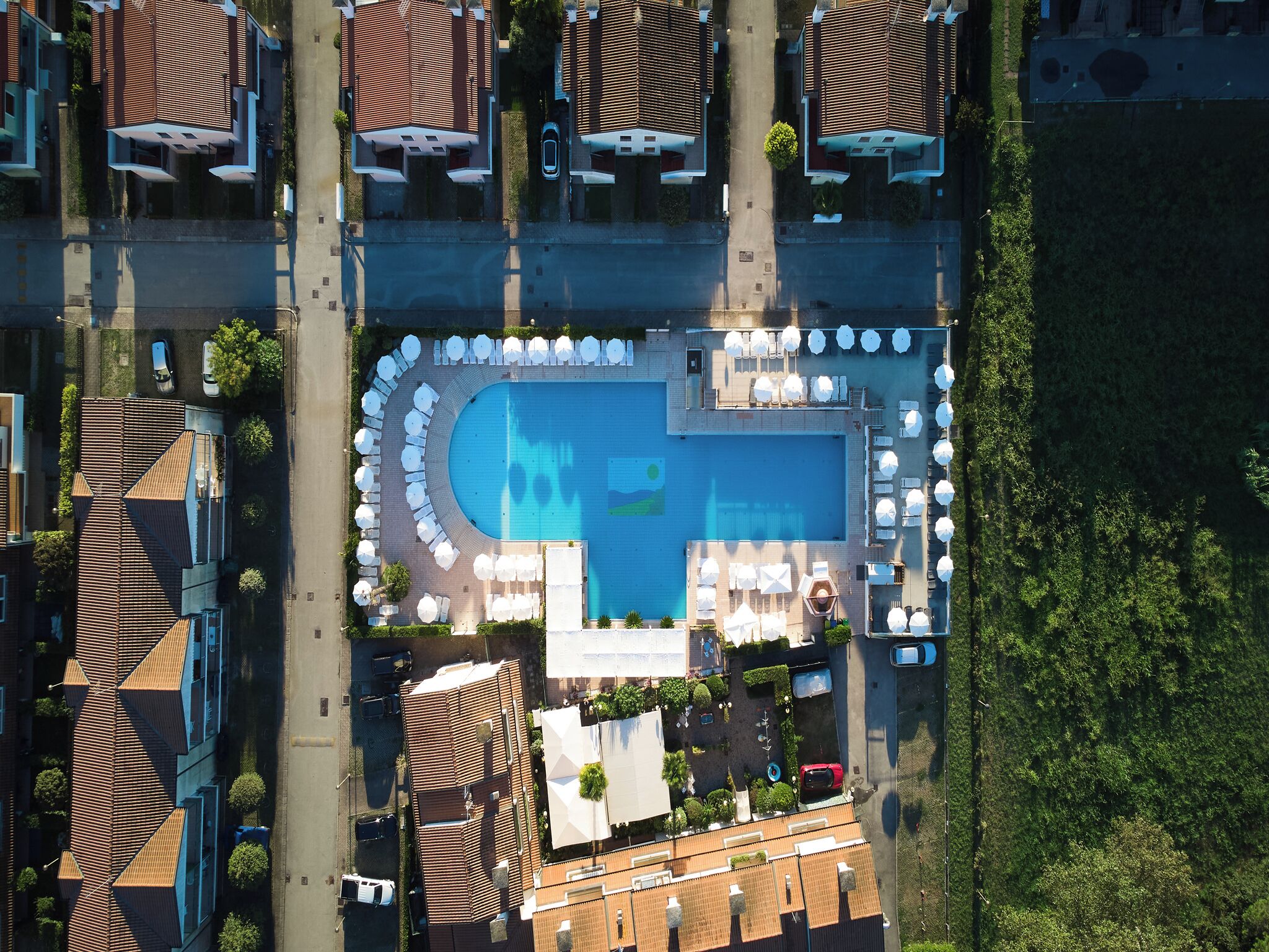 An aerial view of a residential area with a swimming pool surrounded by lounge chairs and umbrellas.