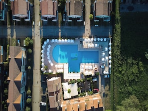 Luftaufnahme einer Wohngegend mit einem Swimmingpool, umgeben von Liegestühlen und Sonnenschirmen.