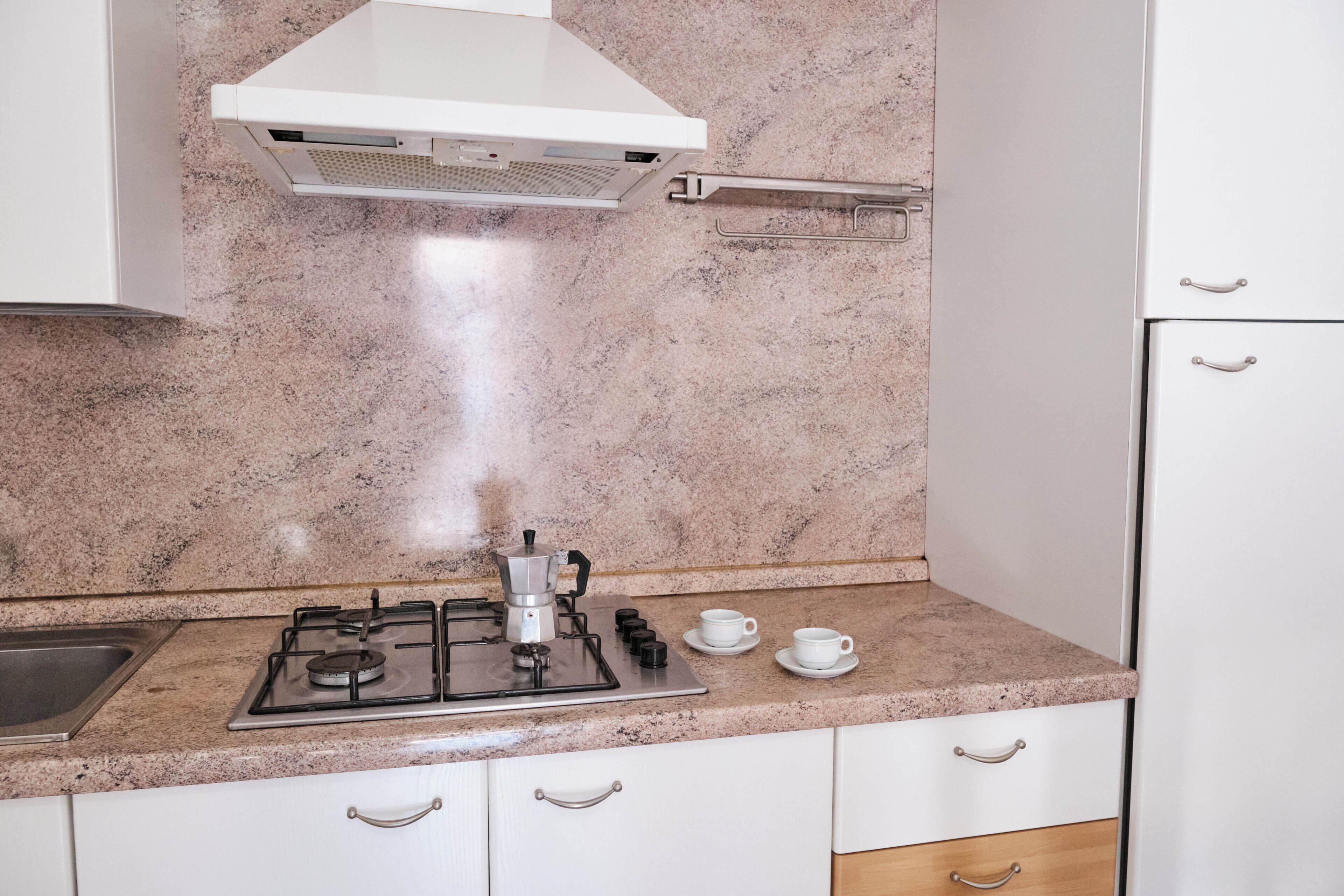 A kitchen with a gas stove, a coffee maker, and two cups on the counter.