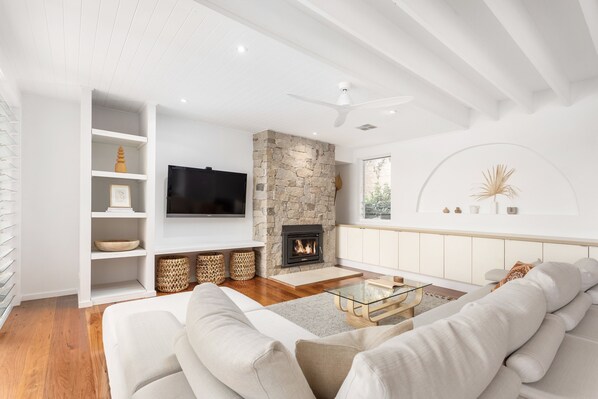 A modern living room with a stone fireplace, white sofas, a glass coffee table, and a flat-screen TV. - Paradise by the lake (Green Point)