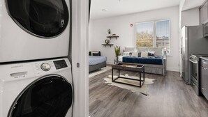 A modern apartment with a laundry area, a living room with a sofa and coffee table, and a kitchen with a refrigerator.