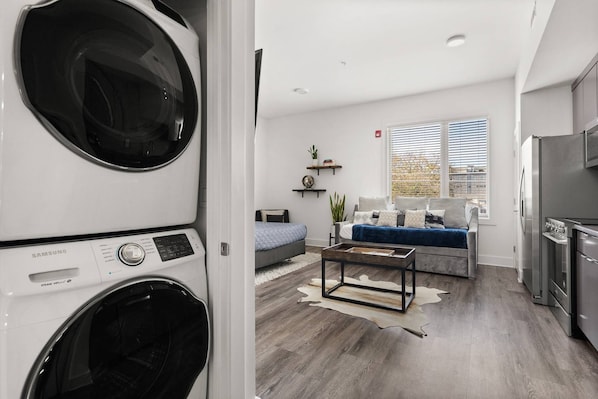 A modern apartment with a laundry area, a living room with a sofa and coffee table, and a kitchen with a refrigerator.