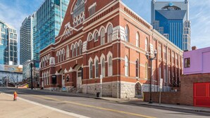 A historic red brick building with arched windows and a prominent clock tower, surrounded by modern skyscrapers.